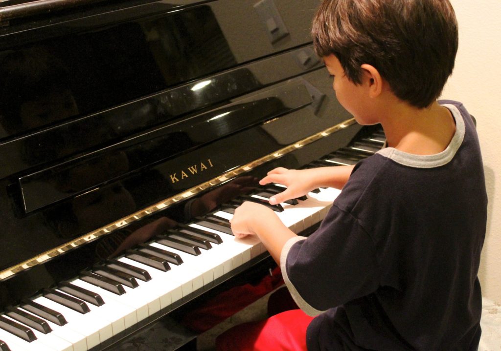 Small boy playing black standup shiny piano